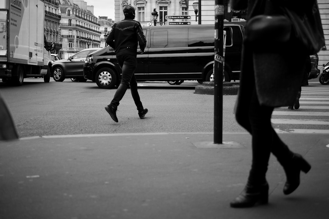 man in black jacket and pants walking on sidewalk in grayscale photography