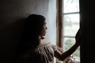 A serene moment of a woman seated by a window, sunlight highlighting the soft texture of her Lumina Apparel blouse.