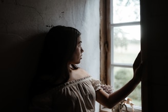Woman wearing a simple, chic outfit standing by a sunlit window.