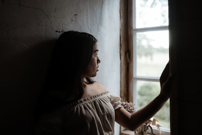 Softly lit photo of a woman in a minimalist, elegant outfit standing by a sunlit window.