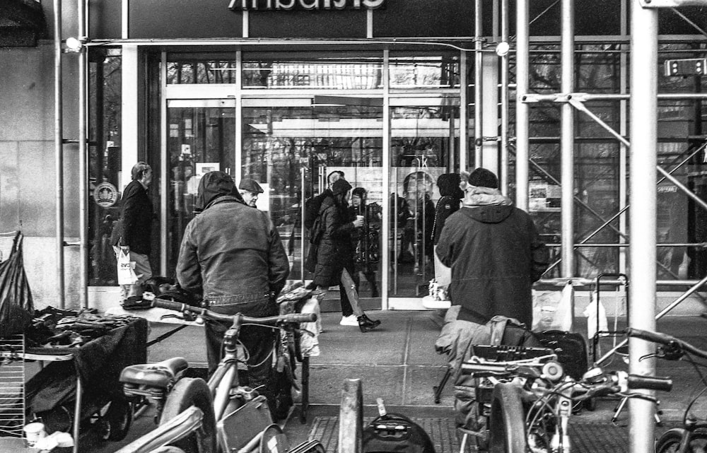 man in black jacket standing beside bicycle in grayscale photography