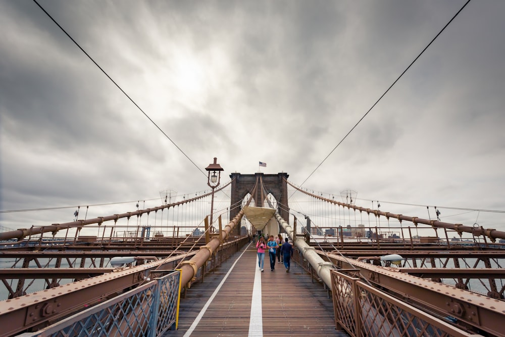 people walking on bridge under cloudy sky during daytime