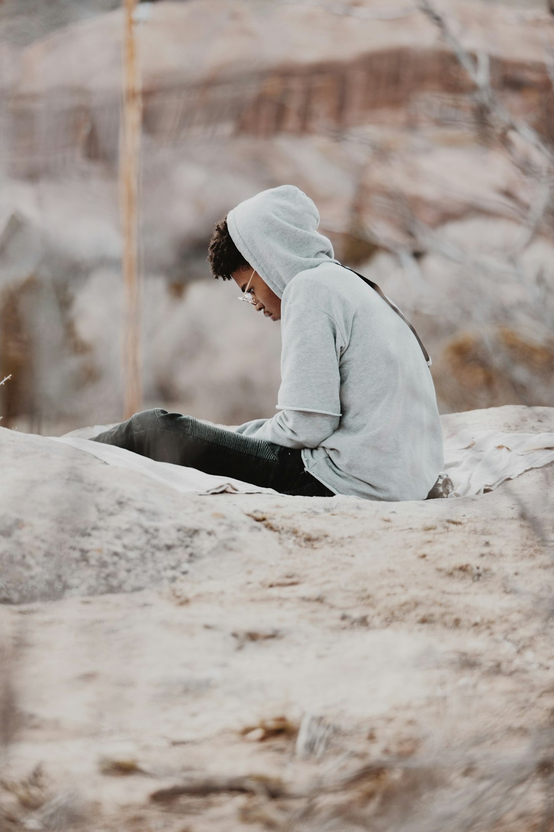 man in gray hoodie and black pants sitting on brown sand during daytime