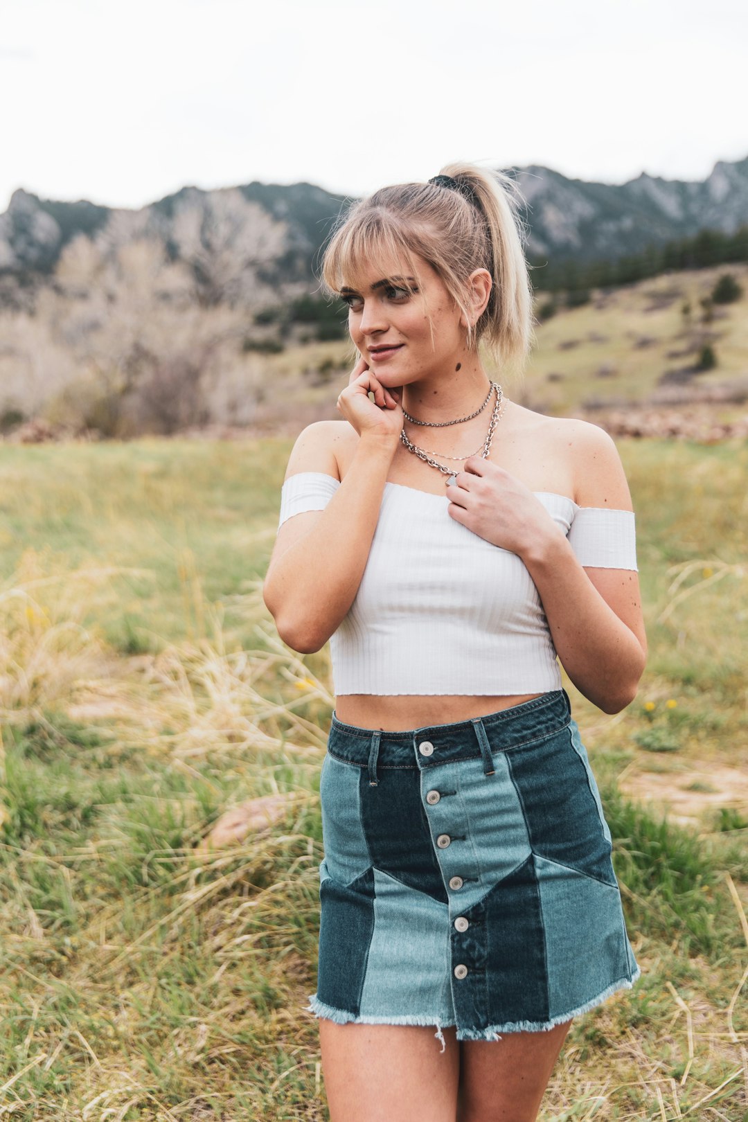 woman in white tank top and blue denim shorts standing on green grass field during daytime