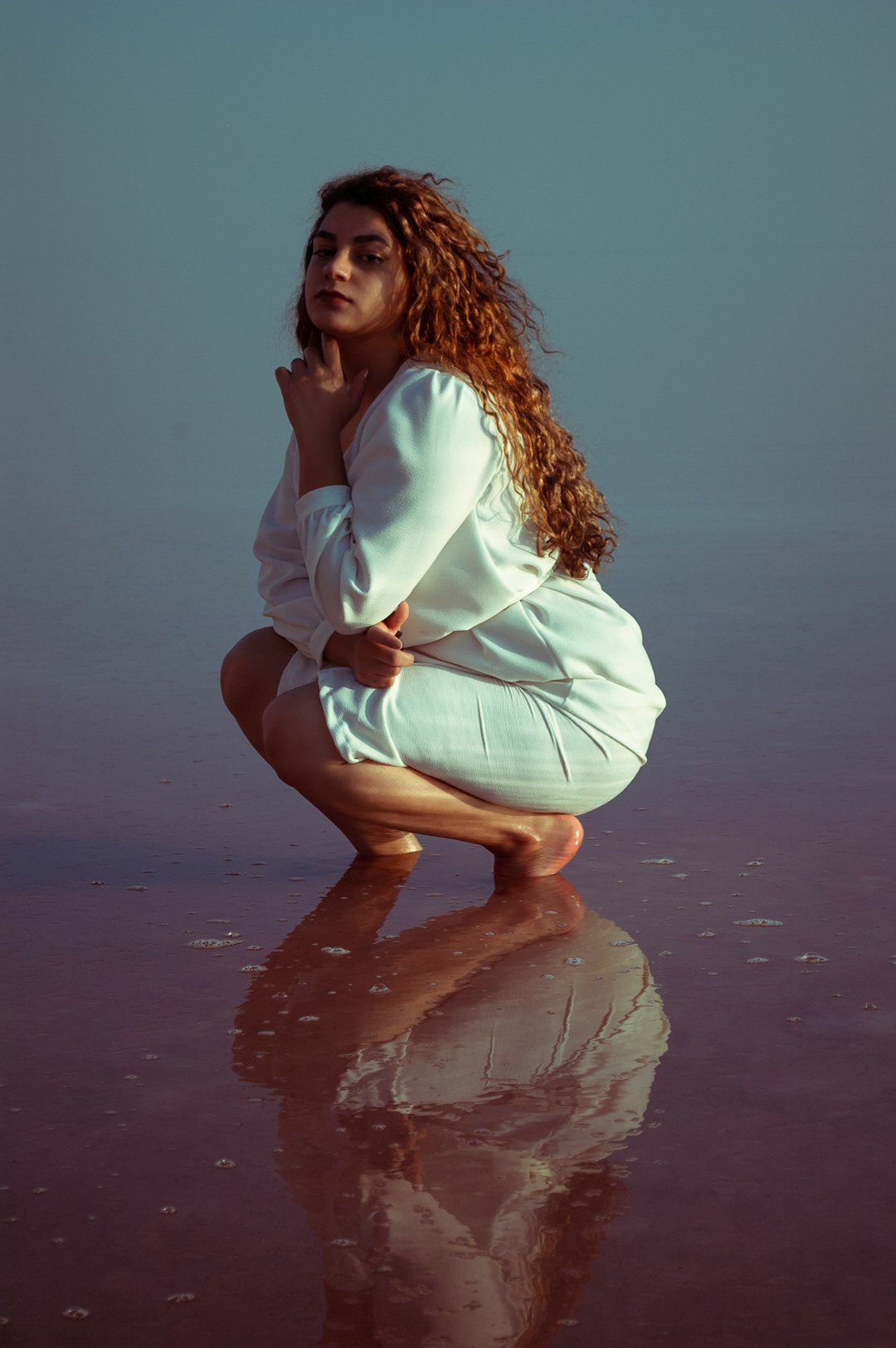 woman in white long sleeve shirt and beige skirt sitting on brown sand during daytime