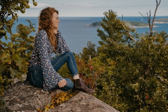 woman in blue and white long sleeve shirt and blue denim jeans sitting on rock near near near near near