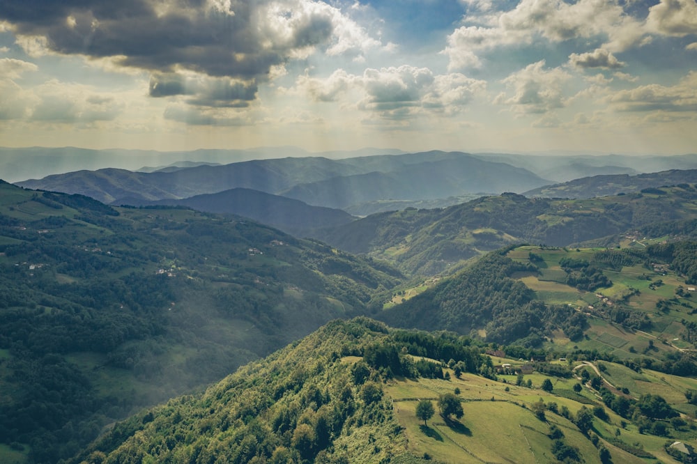 Campo di erba verde e montagne sotto nuvole bianche e cielo blu durante il giorno