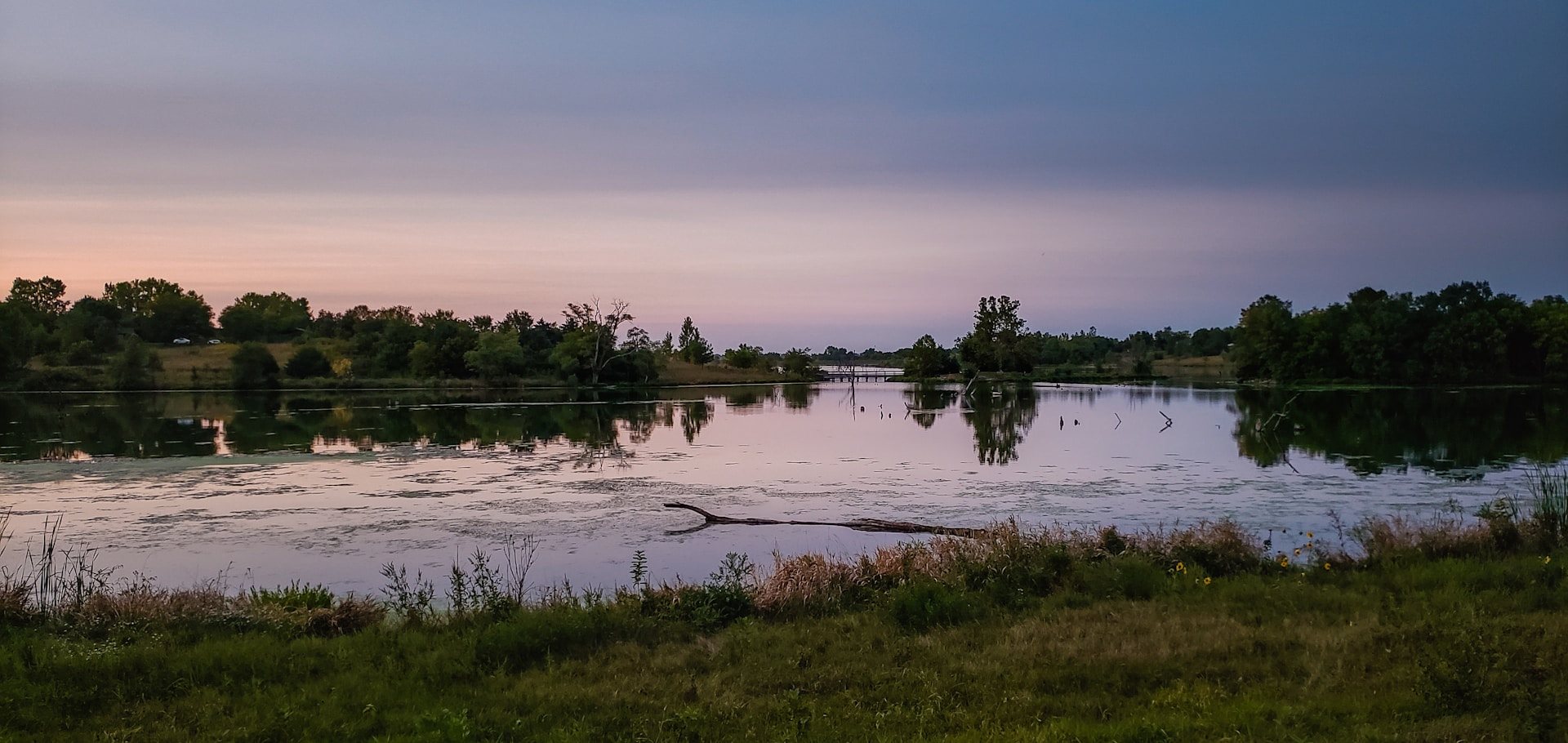 A serene landscape featuring a calm lake reflecting the soft colors of a sunset, evoking a peaceful and contemplative mood.