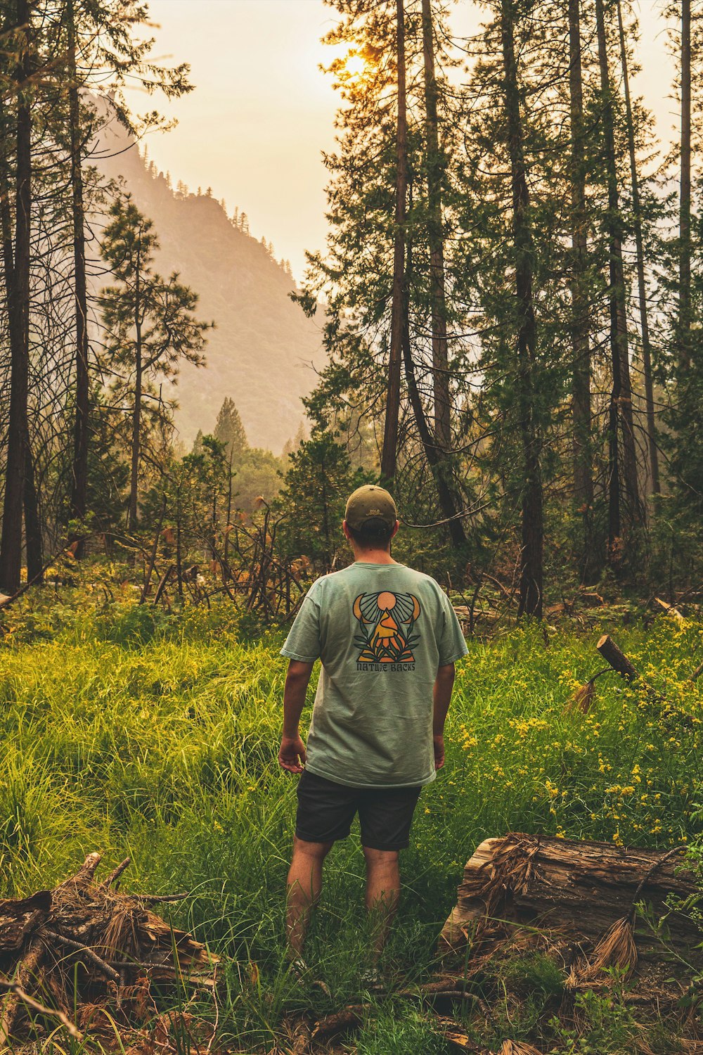녹색 크루 넥 티셔츠를 입은 남자가 나무로 둘러싸인 푸른 잔디밭에 서 있다