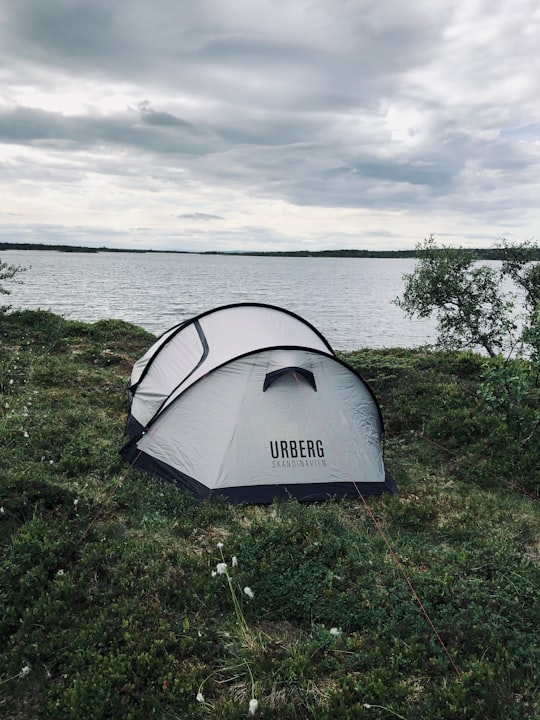 white dome tent on green grass field near body of water during daytime in Fulufjället Njupeskär Sweden