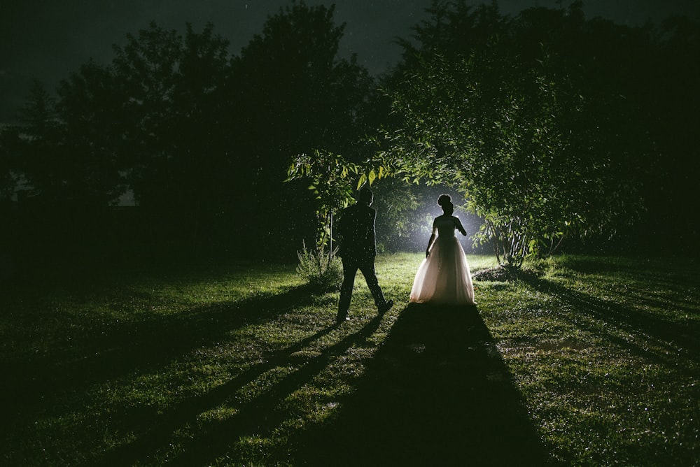 man and woman walking on pathway between trees during nighttime