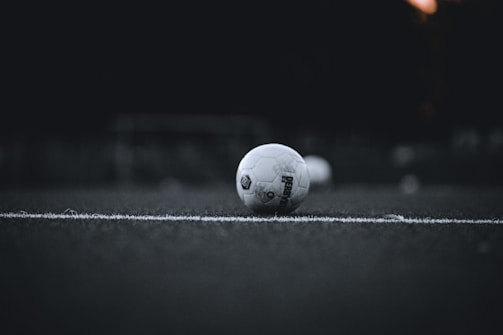 Minimalist black and white shot of a soccer ball on a wet field.