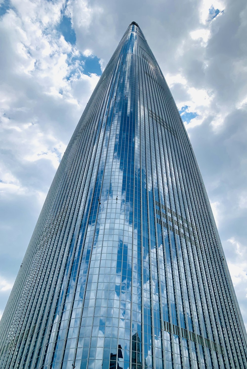 낮에는 흰 구름과 푸른 하늘 아래 파란색과 흰색 유리 벽으로 둘러싸인 고층 건물