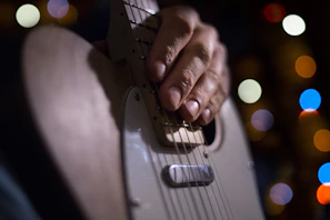 A close-up of a guitar being played on stage with colorful stage lights in the background.