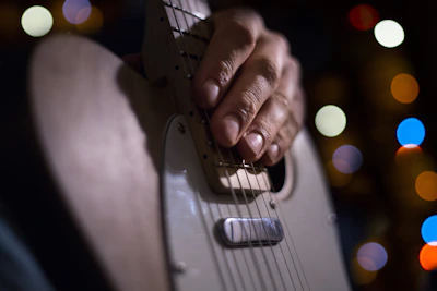 Close-up of a guitarist’s hand strumming funky electric guitar strings under warm stage lights.