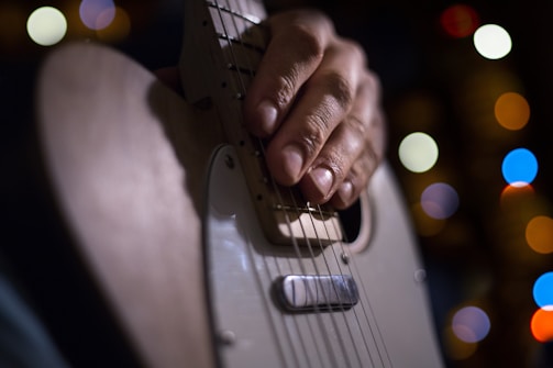 Close-up of hands playing a guitar with colorful stage lights in the background.