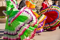 Vibrant dancers in traditional Mexican attire perform, their colorful skirts swirling in mid-motion. The focus is on the detailed patterns and bright colors of their outfits.