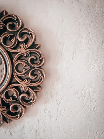 An ornate, metallic frame with intricate, swirling patterns is visible on the left side, set against a textured, off-white wall.