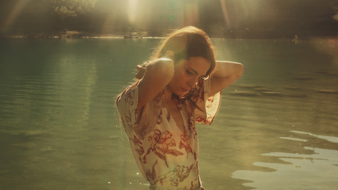 woman in white and brown floral shirt standing near body of water during daytime