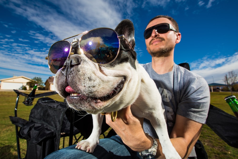 man in black sunglasses holding white short coated dog