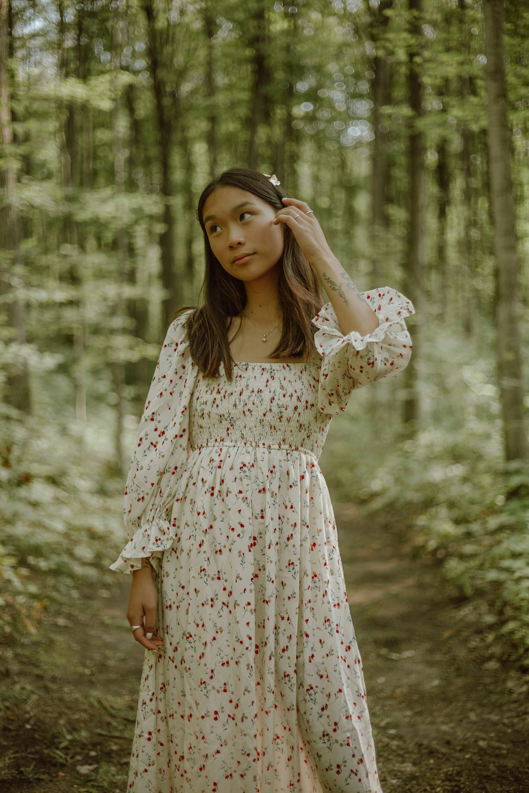 woman in white and red floral dress standing near trees during daytime