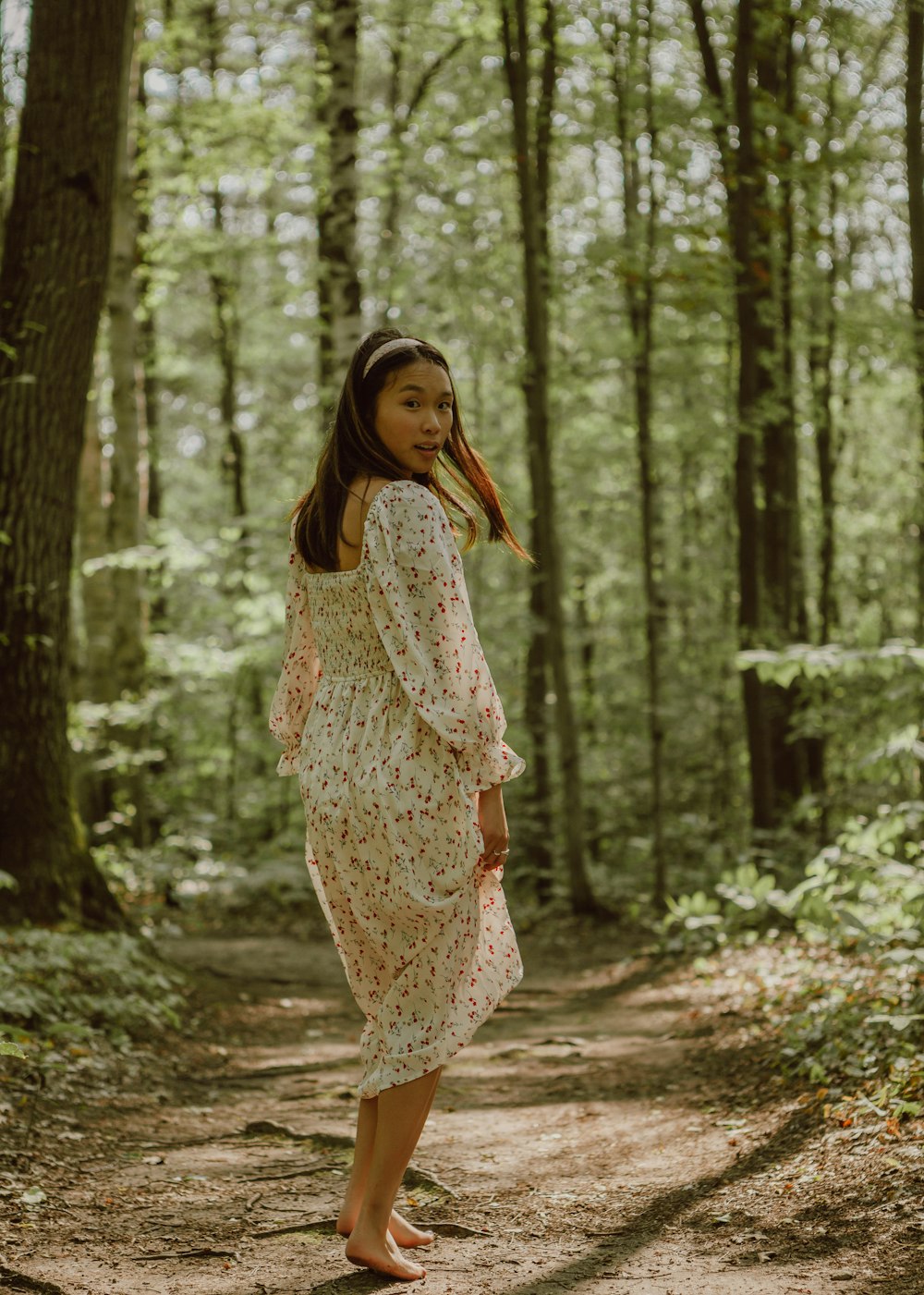 woman in white and brown floral dress standing in forest during daytime
