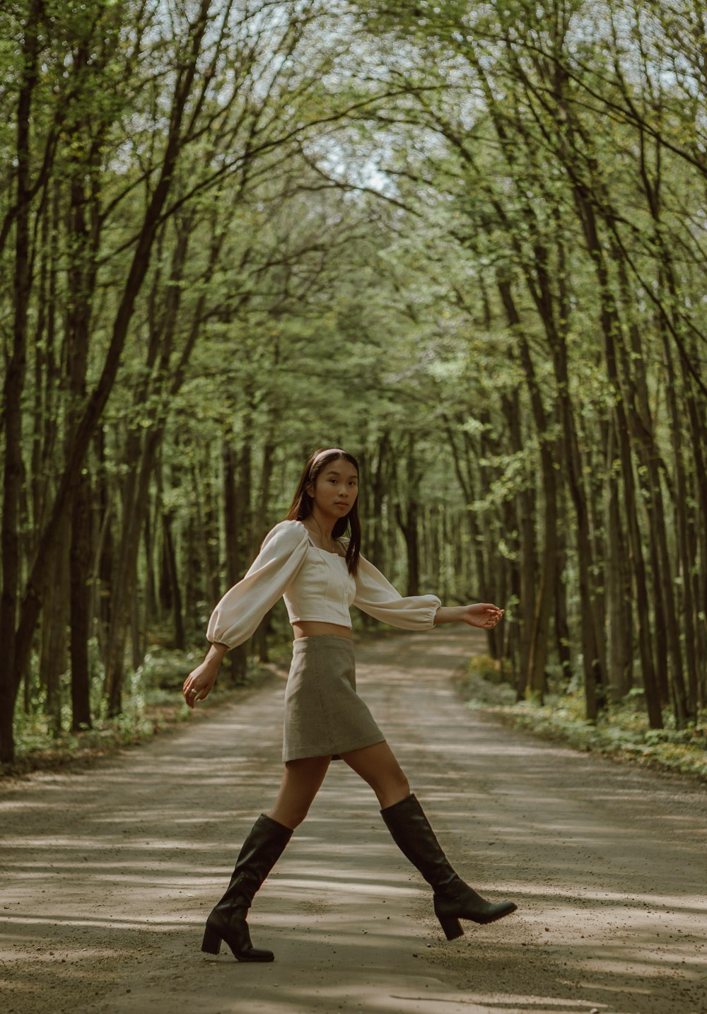 woman in white long sleeve shirt and black skirt standing on gray asphalt road between green