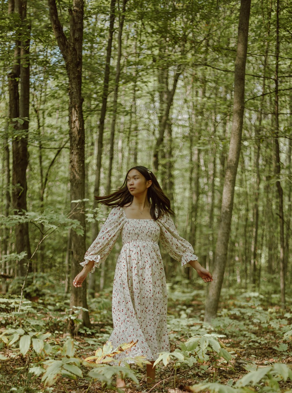 woman in white and black floral dress standing in forest during daytime