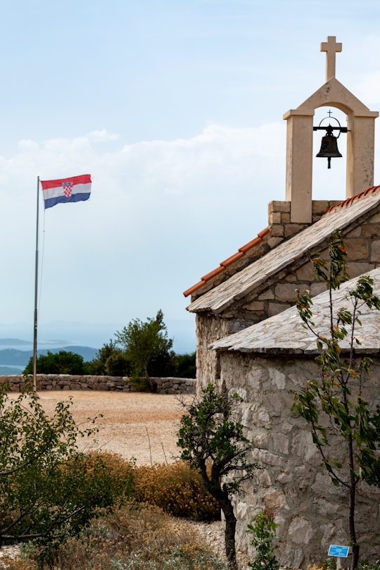 brown and white concrete building with bell flag on top in Vransko jezero Croatia