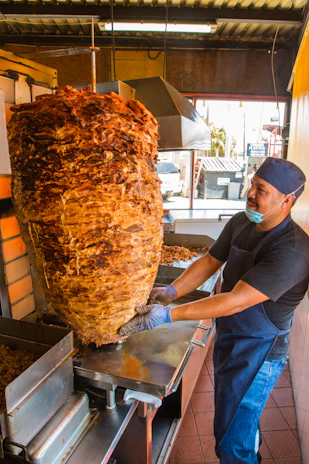Close-up of sizzling pastor tacos cooking on a vertical spit with vibrant spices.