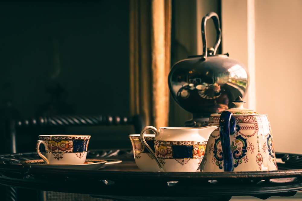 white and blue floral ceramic teacup on saucer beside black and white floral ceramic teapot