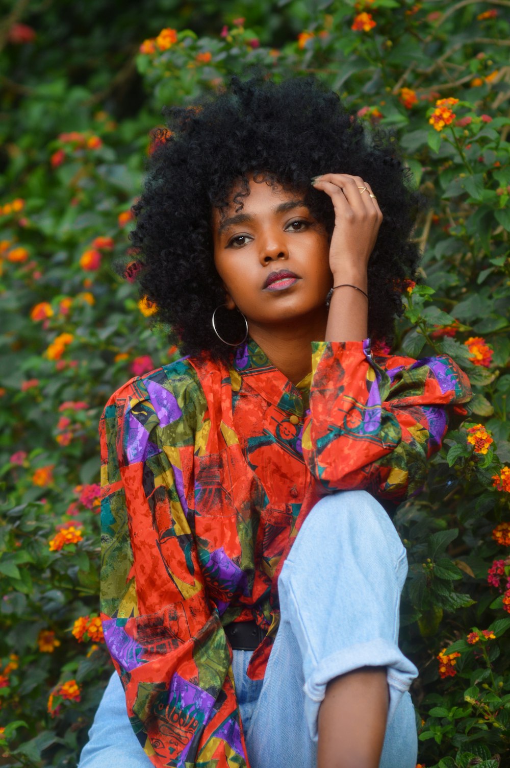 woman in orange and blue floral button up shirt standing near red flowers