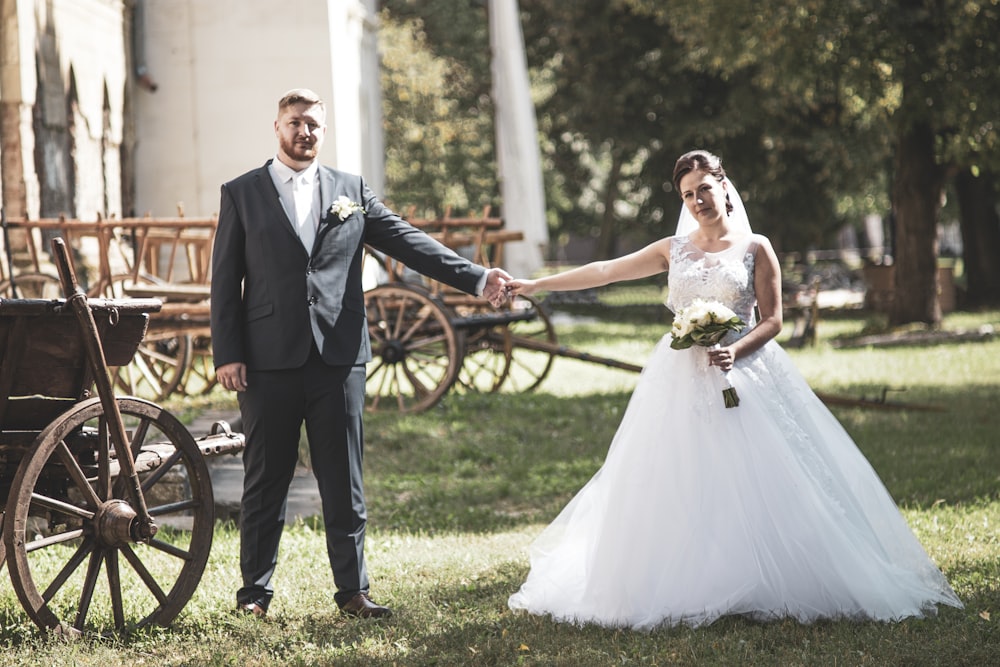 man in black suit holding woman in white wedding dress on green grass field during daytime