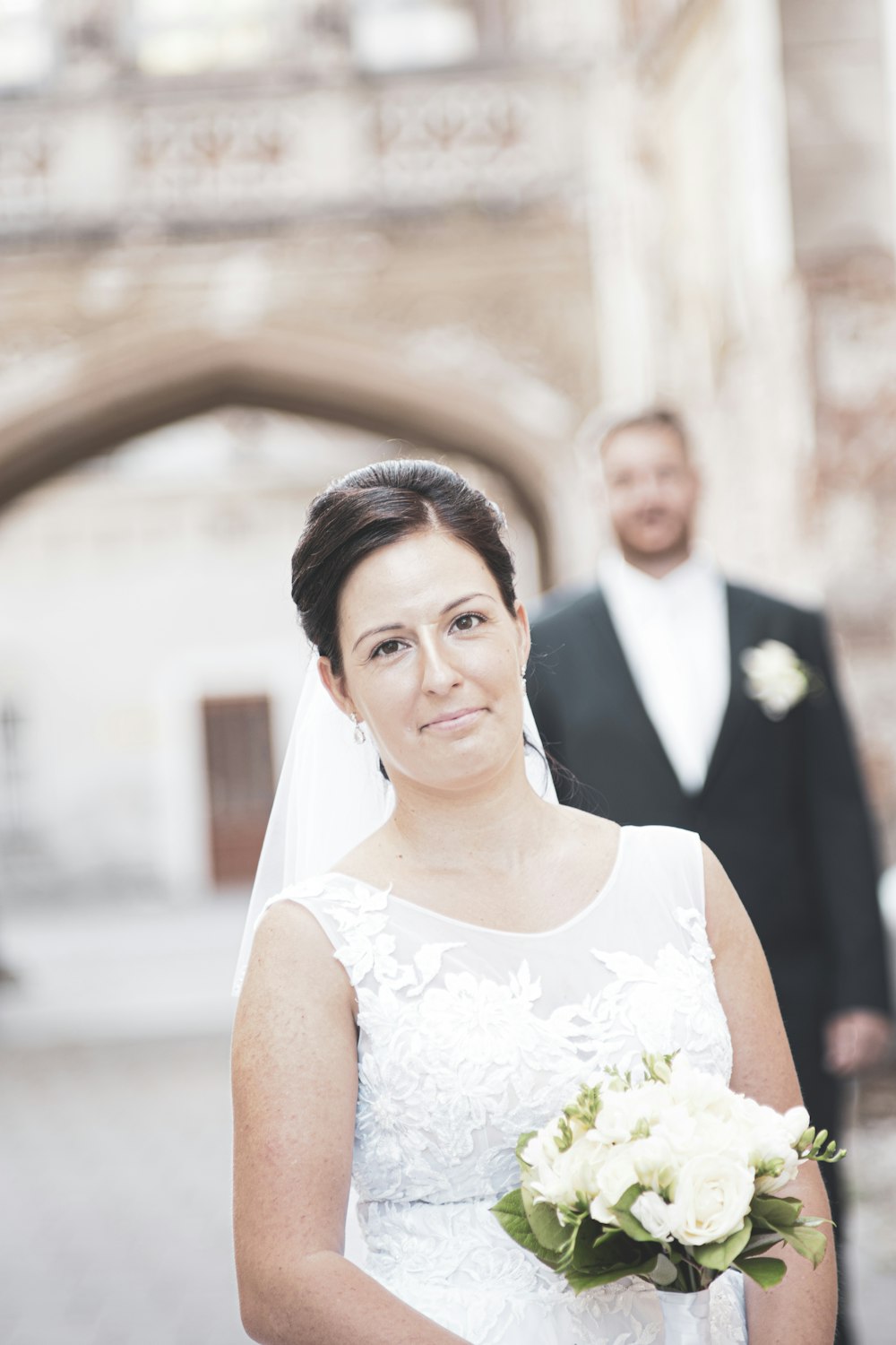 woman in white floral lace sleeveless dress smiling beside man in black suit