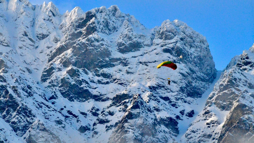 person in yellow parachute over snow covered mountain