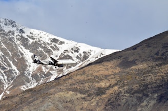 Airplane flying over a scenic mountain landscape at sunset.