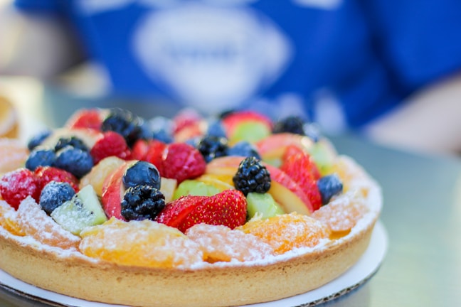 A vibrant fruit tart topped with glistening berries and a light dusting of powdered sugar.