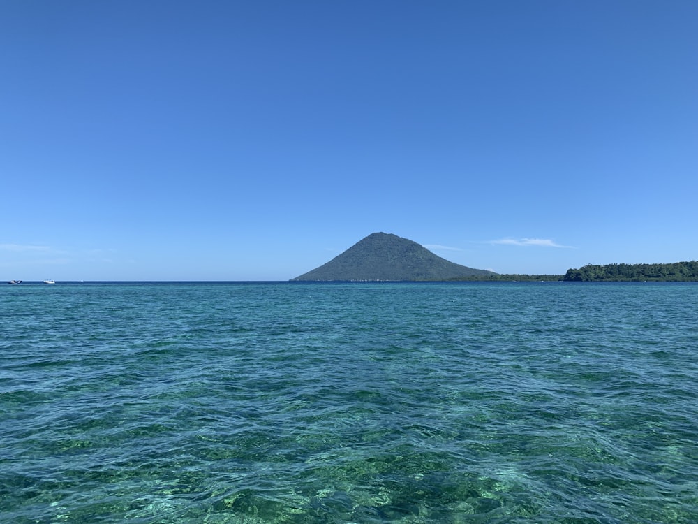 green sea near mountain under blue sky during daytime