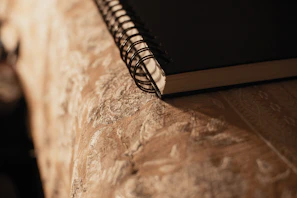 Close-up of a sleek, matte black leather notebook resting on a polished wooden desk with soft natural light.