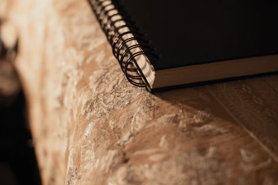 A close-up of hands holding a warm beige journal with soft gold accents, resting on a navy fabric background.