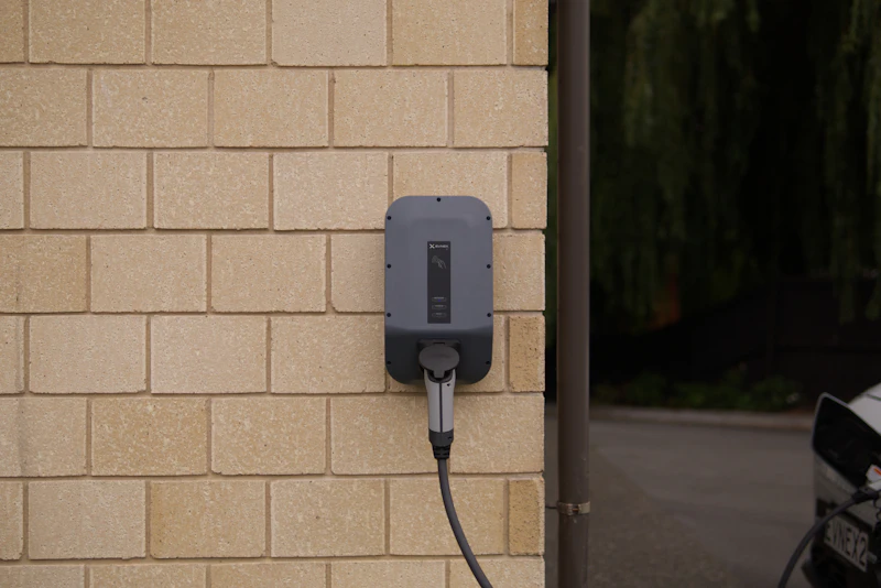 Grey wall-mounted 7 kW EV charge point on a pale brick wall with its cable hung on the hook
