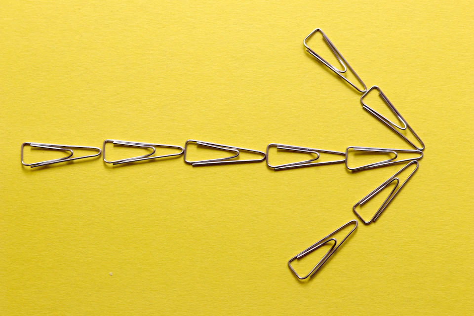 Silver paper clips form an arrow shape on yellow background, pointing upwards slightly