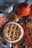 A freshly baked pie with a decorative braided lattice crust sits on a wooden surface surrounded by autumn leaves, a small pumpkin, acorns, and a metal coffee pot on a fabric cloth.