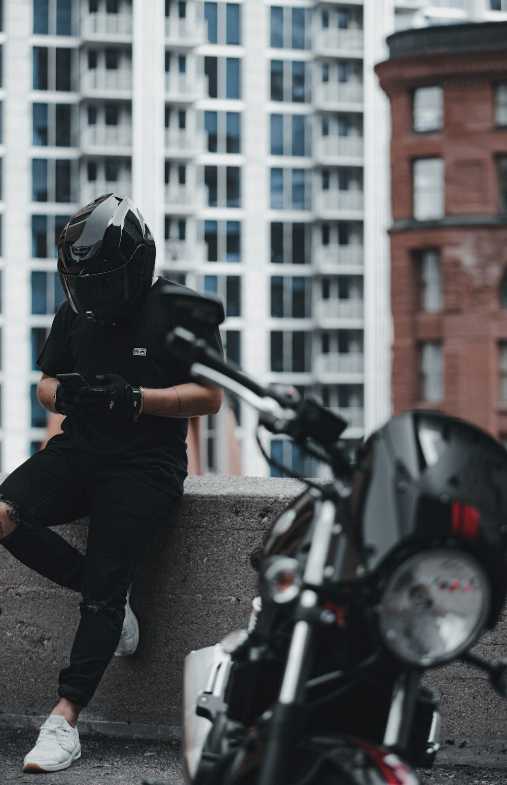 검은 재킷과 회색 바지를 입은 남자는 낮에 오토바이를 타고 검은 헬멧을 쓰고