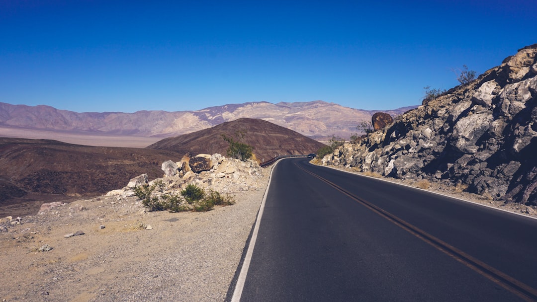 gray asphalt road near brown mountain under blue sky during daytime