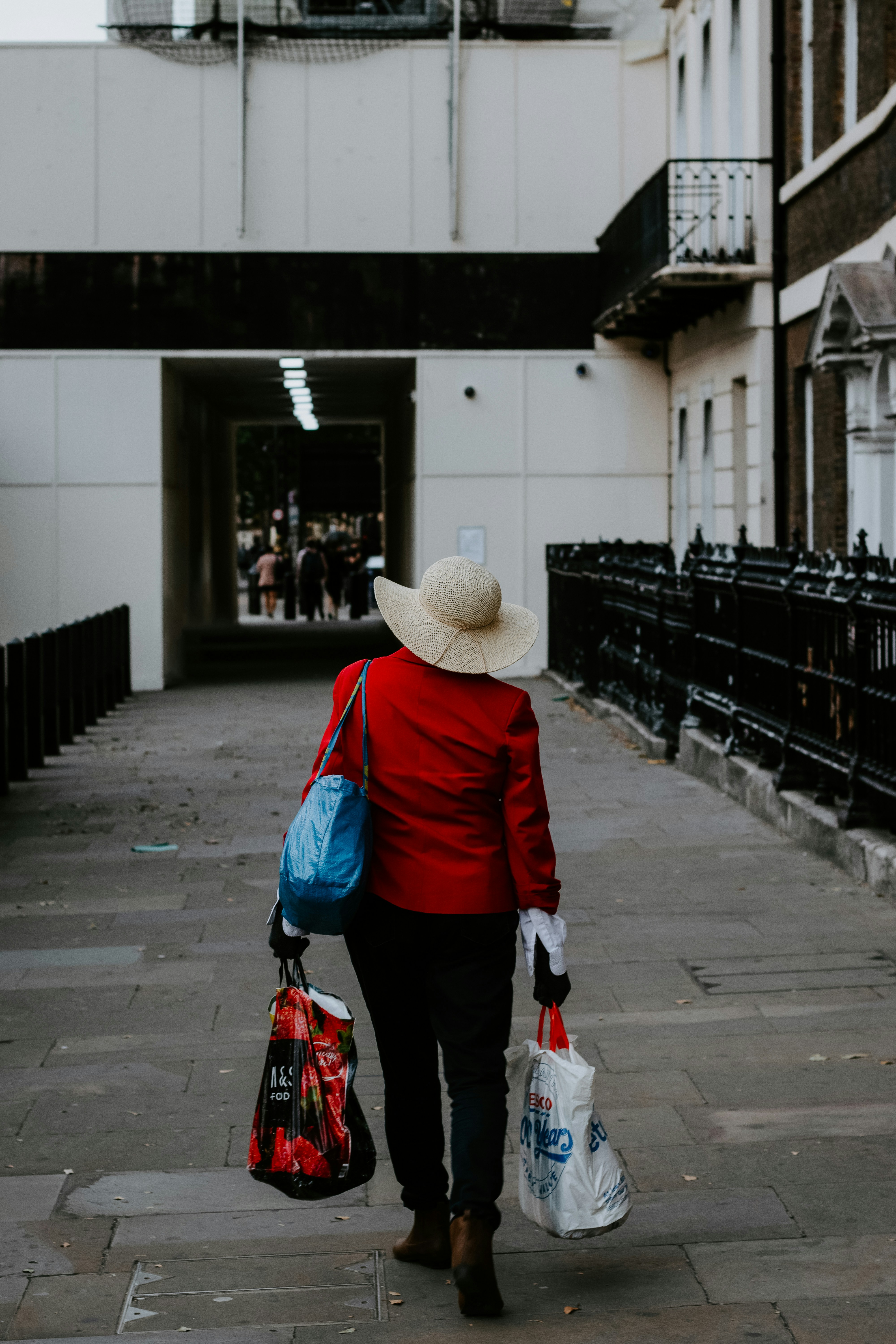 person in red jacket and black pants wearing brown hat walking on sidewalk during daytime