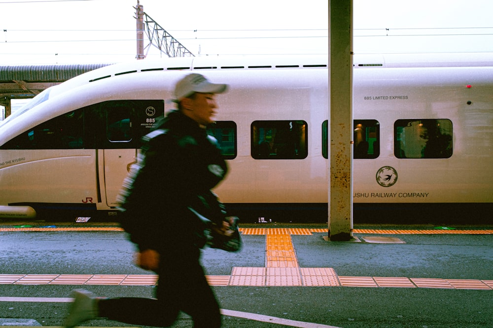 man in green jacket and black pants sitting on gray concrete road beside white train during