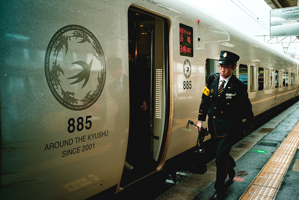 man in black jacket and black pants standing beside white and black train