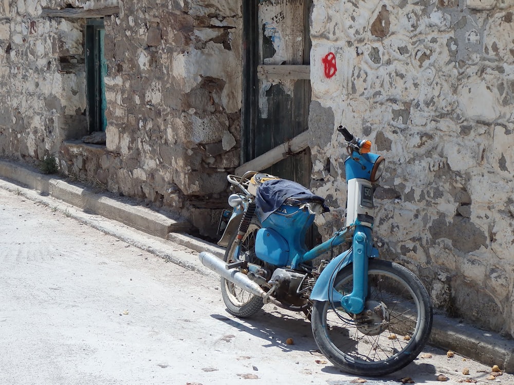 blue motorcycle parked beside brown concrete building during daytime