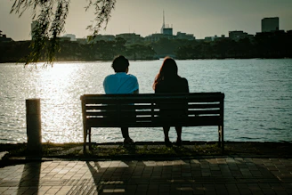 2 person sitting on bench near body of water during daytime